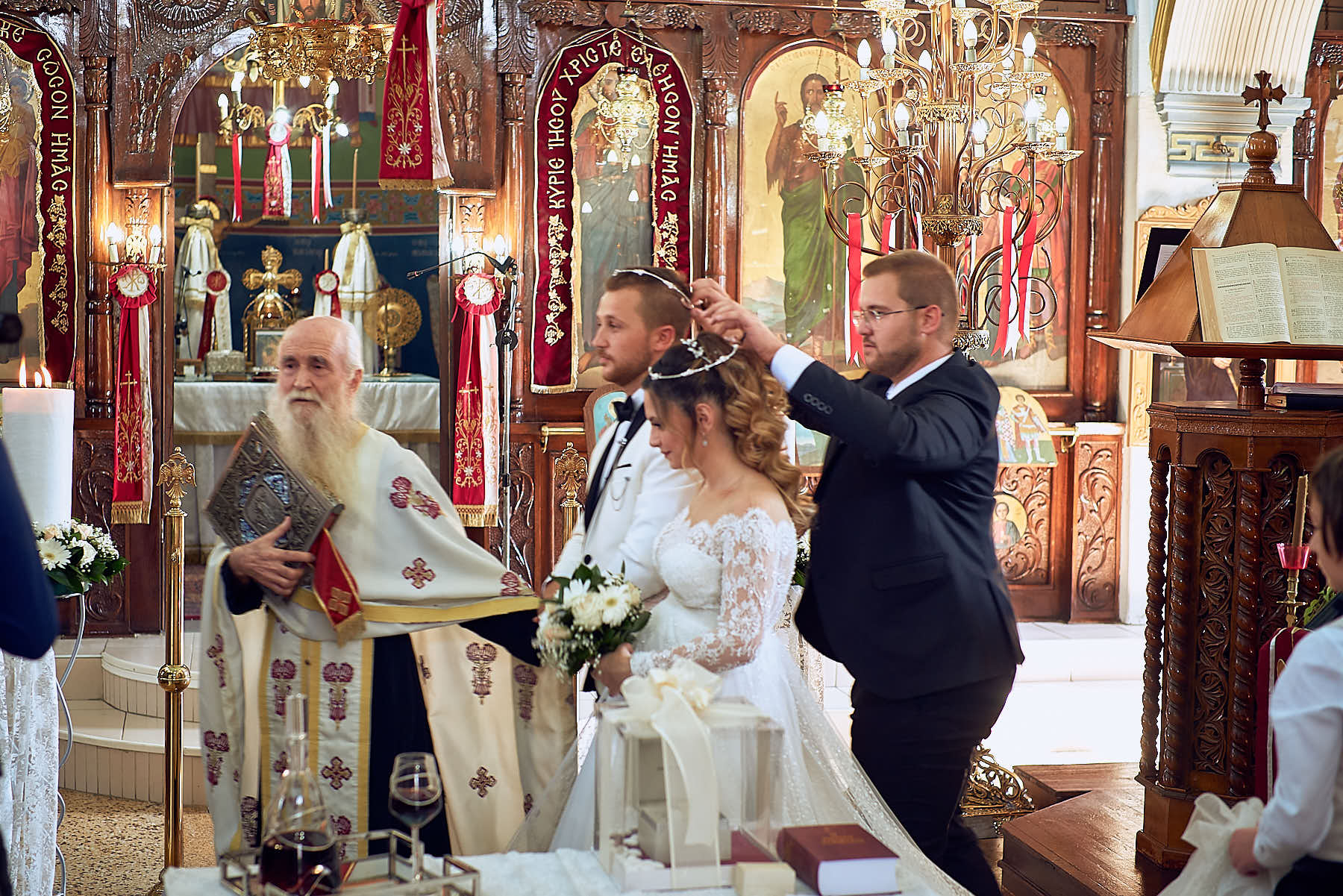 Groom, bride, friend (putting wedding crowns) and priest in the church, religious pictures