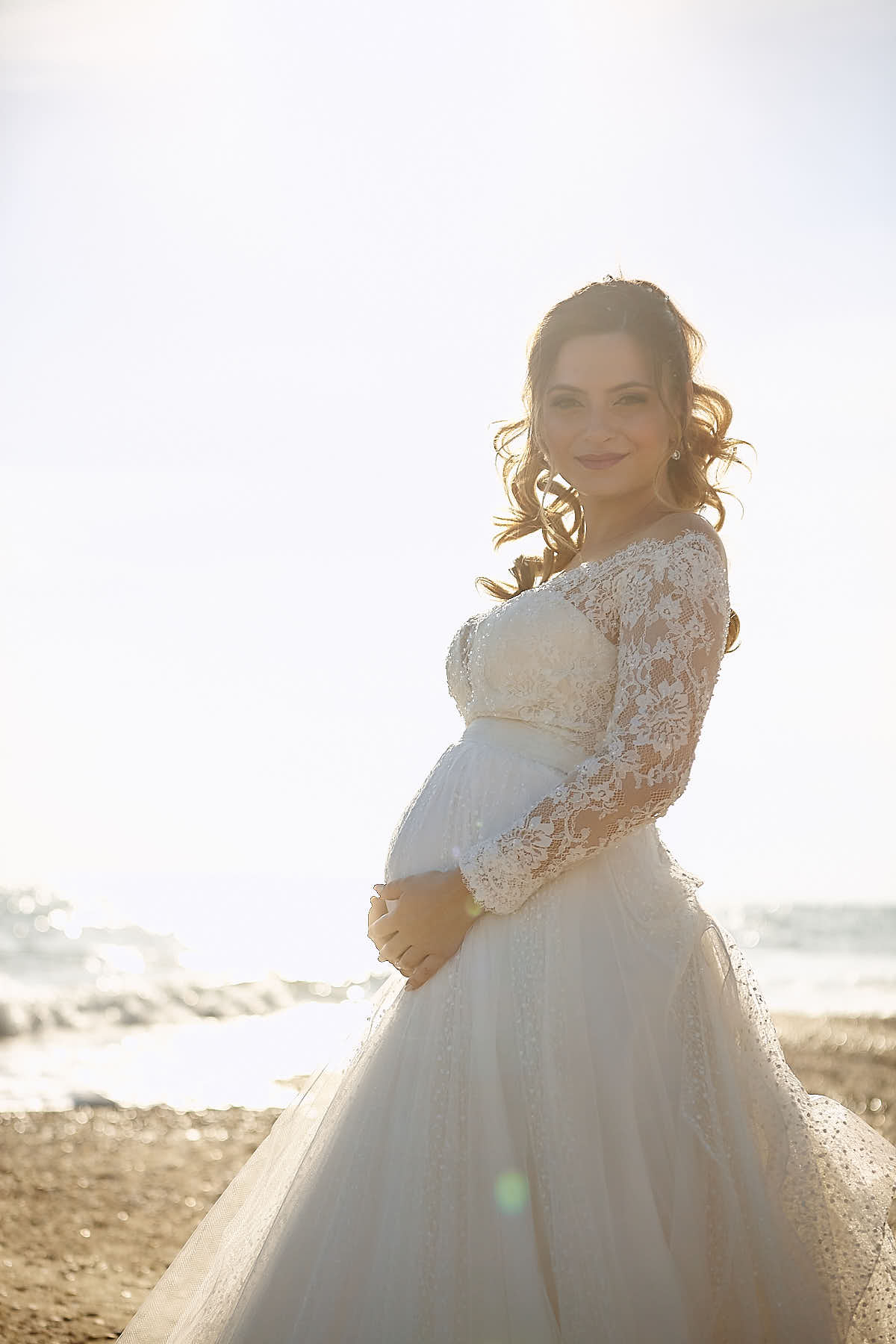 Bride holding her growing belly while looking at the camera with a pure smile