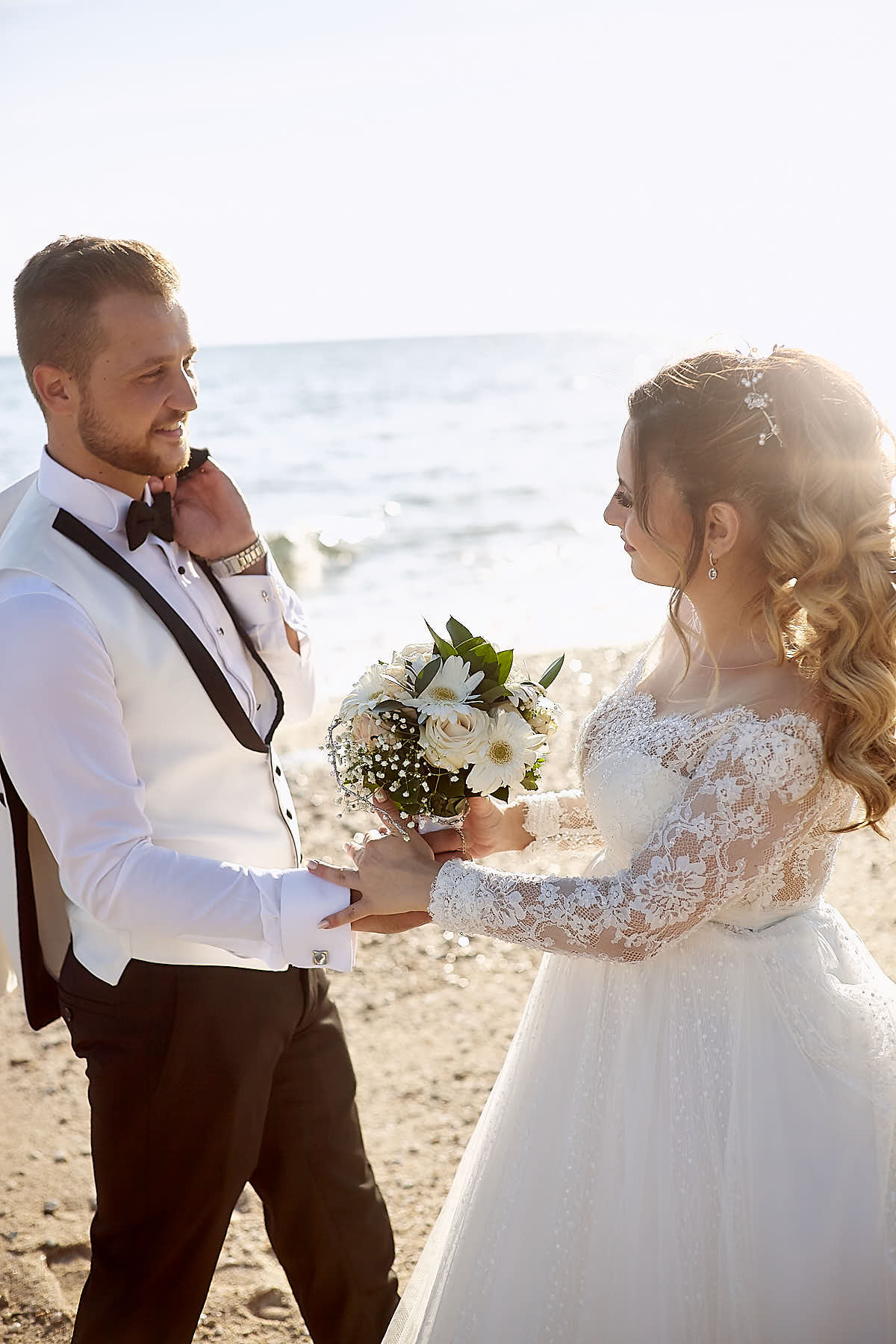 Groom holding the bouquet with his bride while looking at her