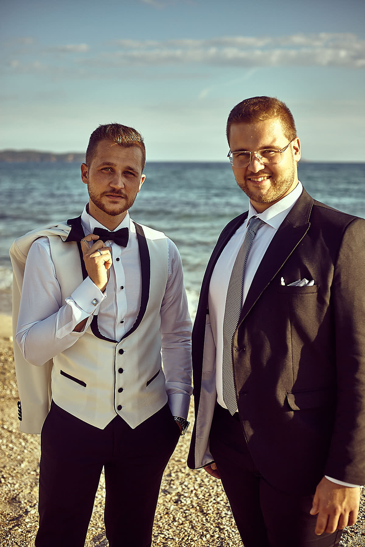 Groom with his jacket on his shoulder with a relative besides him, sea and sky on the background