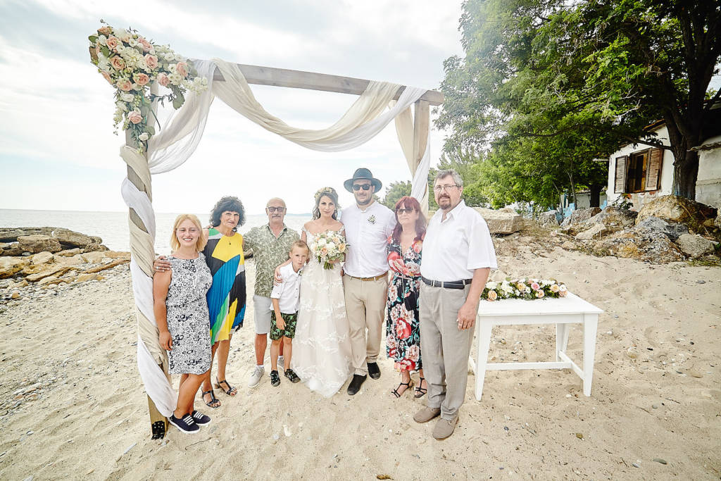 Family posing under the wedding arch for a family photo at the beach in Halkidiki