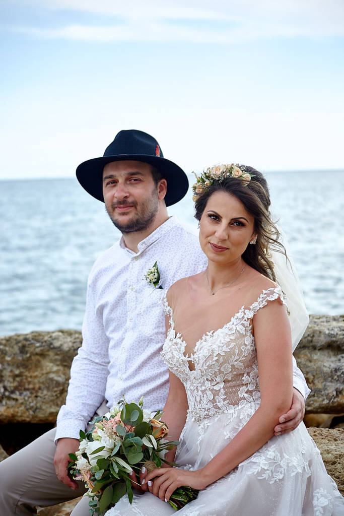 Groom and bride posing for a photo while sitting on a rock